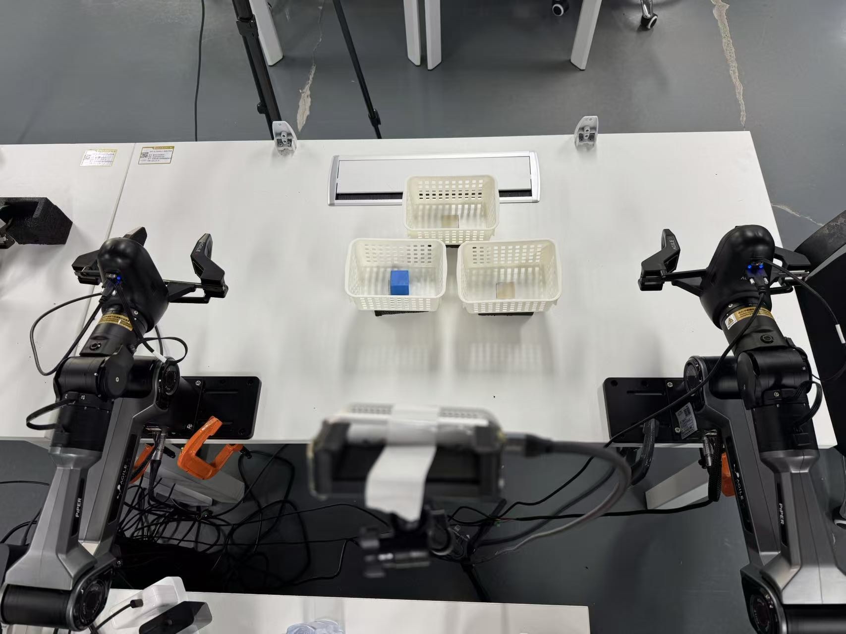 Overhead view of the dual-arm cell at Put Back initial state. A blue block sits in a side tray before the histories diverge.