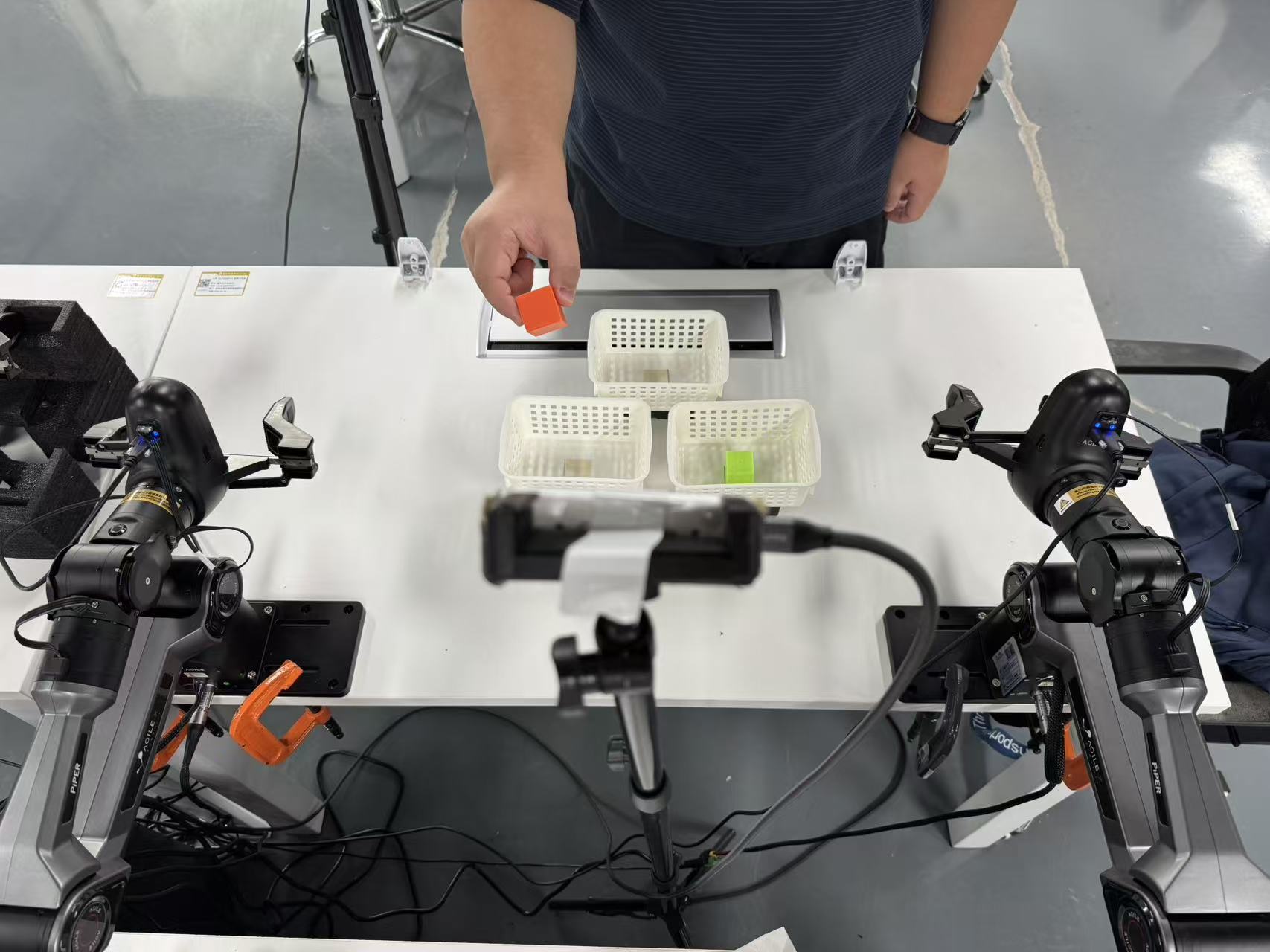 Dual-arm cell during Repick. A person holds an orange block above the trays.